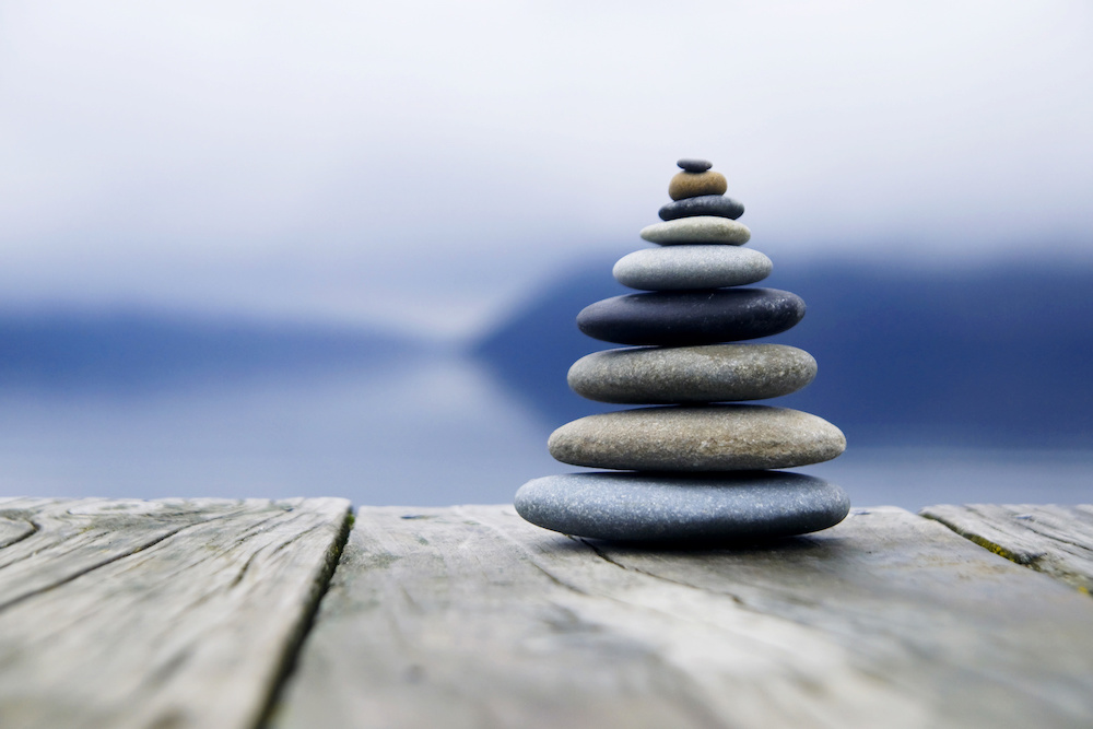Stack of balanced stones on wooden dock with blurred water and mountains in background