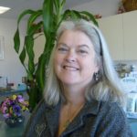 Dr. Mary Jane Doyle smiling in her office, with a vase of pansies and a tall corn plant behind her